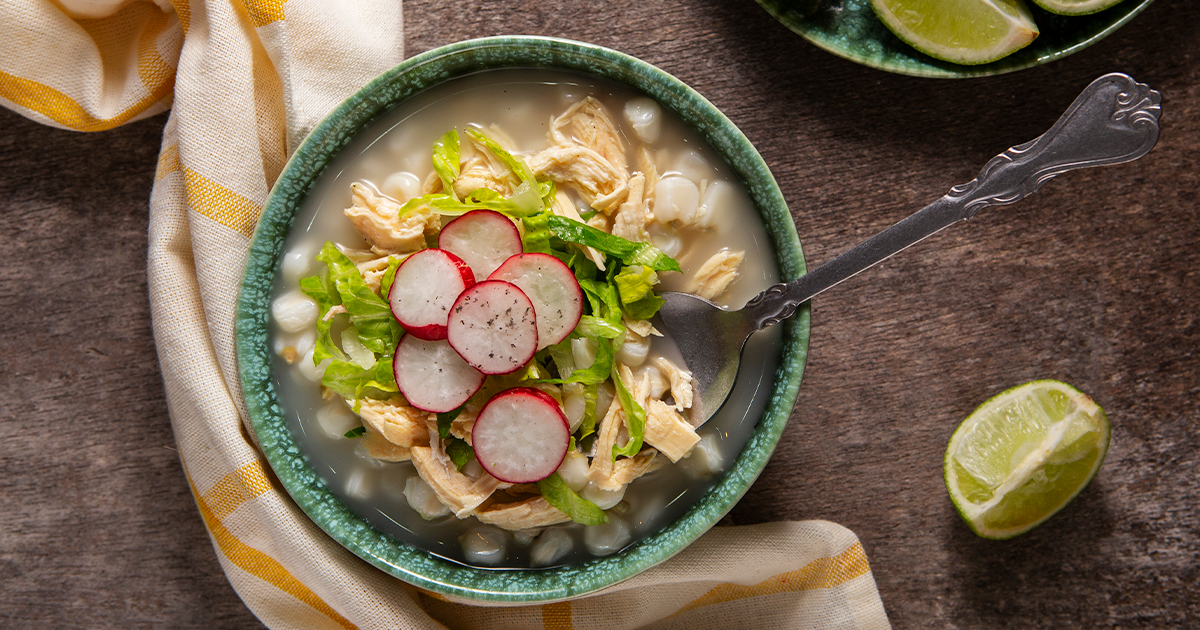 Receta de pozole blanco tradicional servido con lechuga, rábano y tostadas
